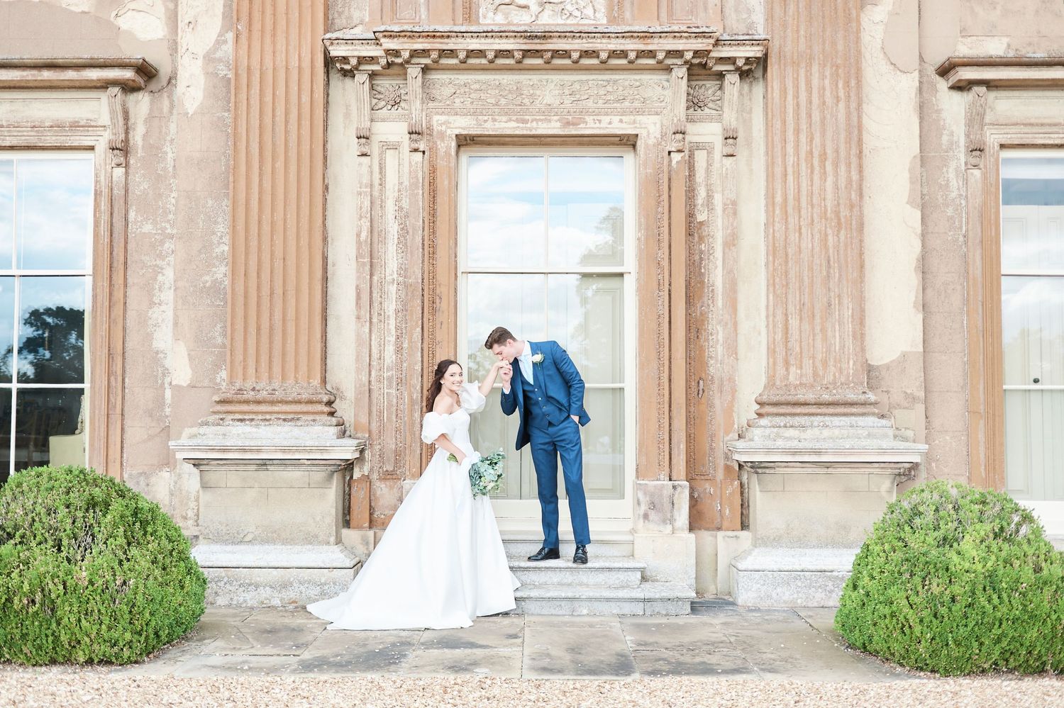 groom kisses brides hand on the steps of Turvey house in buckinghamshire by Norfolk's award winning wedding photographer