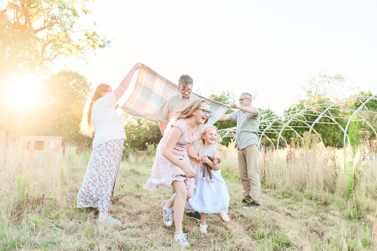 children run under blanket as parents throw it into the air at sunset. by award winning Norwich photographer Faye Amare