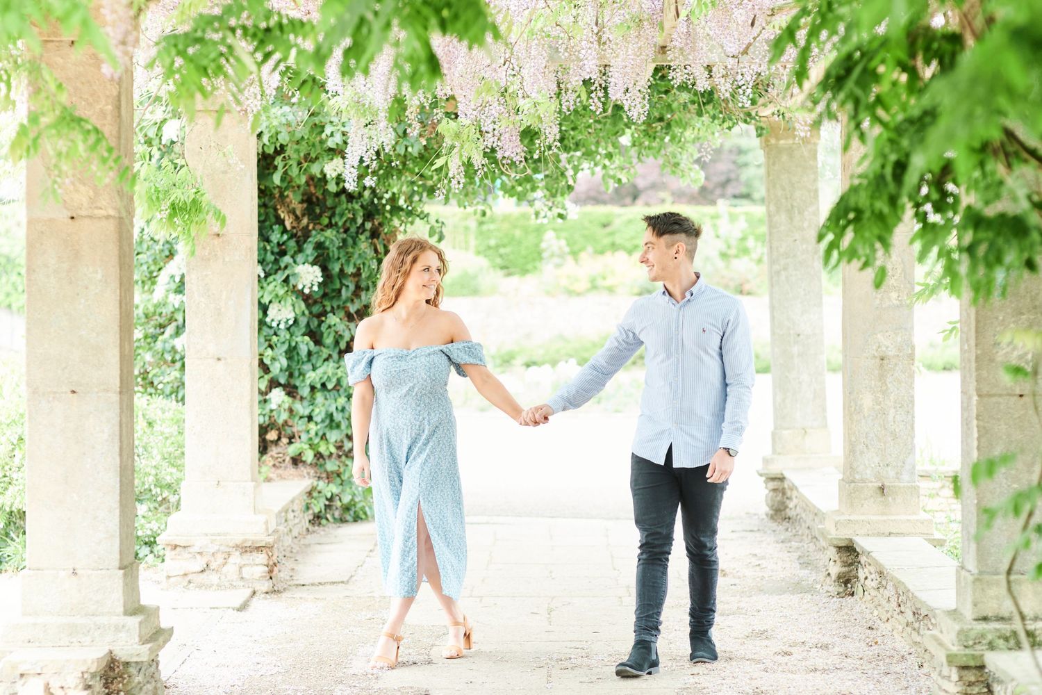 couple walk under the wisteria arch at Waterloo Park in Norfolk by Norwich's best family photographer Faye Amare