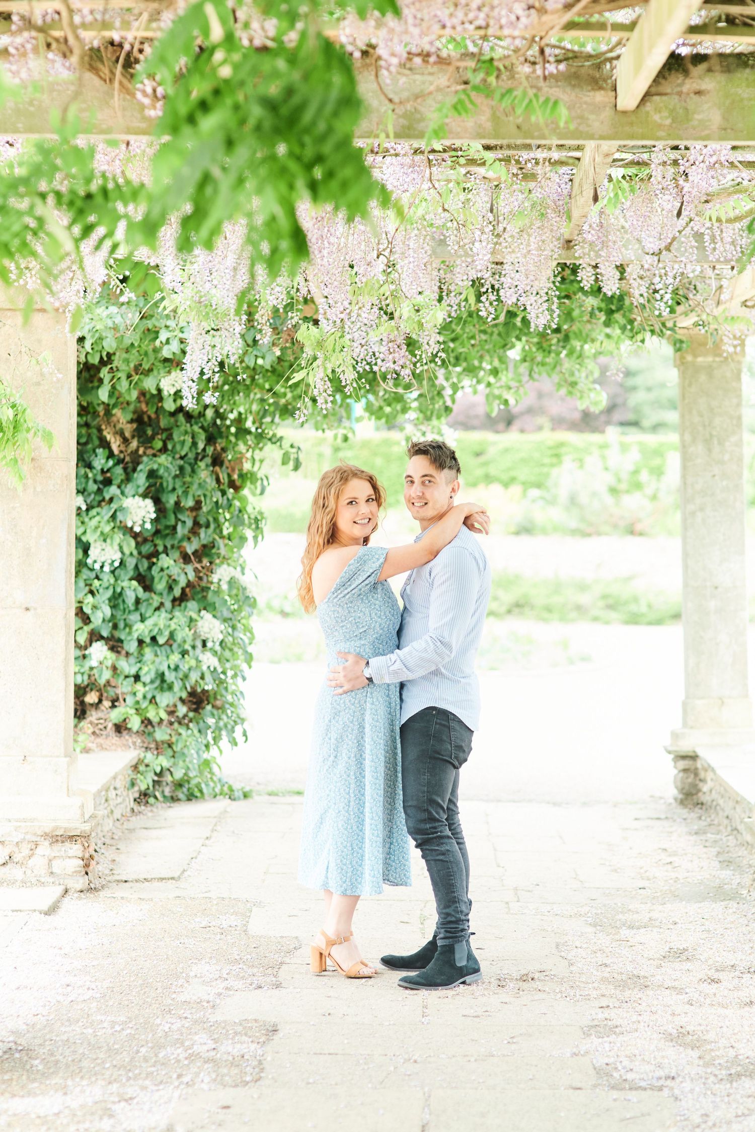 couple cuddle under the wisteria arch at Waterloo Park in Norfolk by Norwich's best family photographer Faye Amare