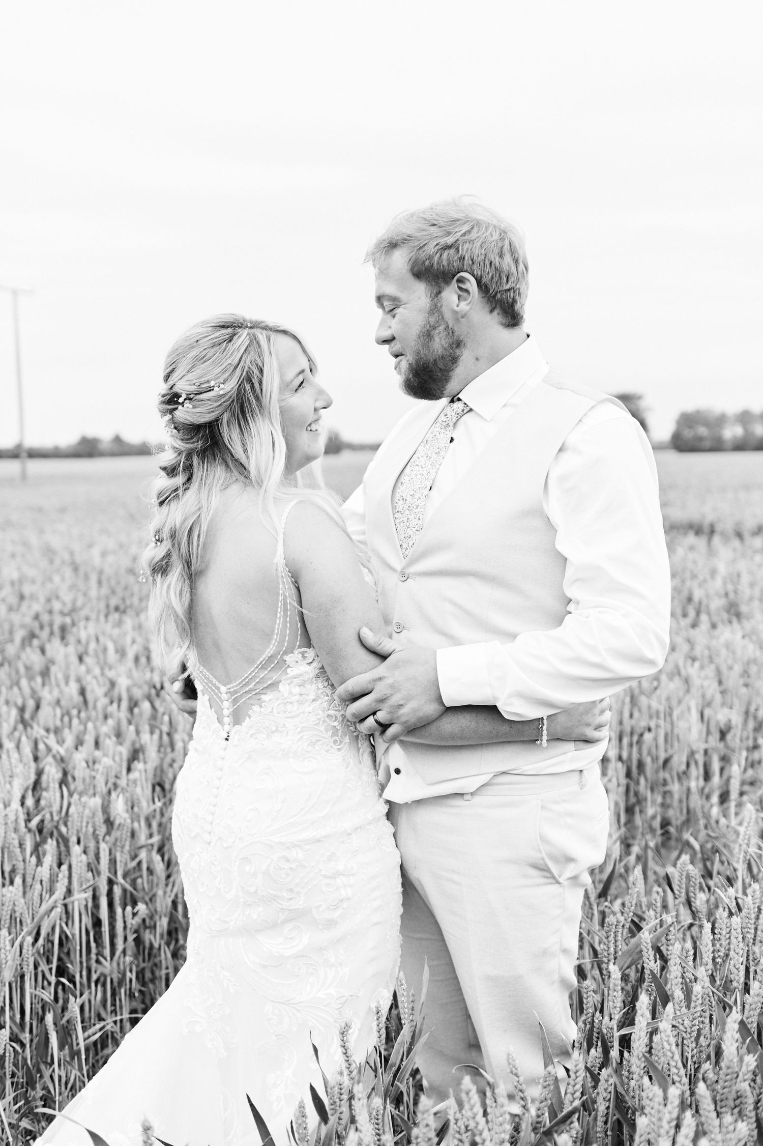 bride & groom cuddle in wheat fields at Curds Hall Barn, Norfolk. by award winning wedding photographer Faye Amare