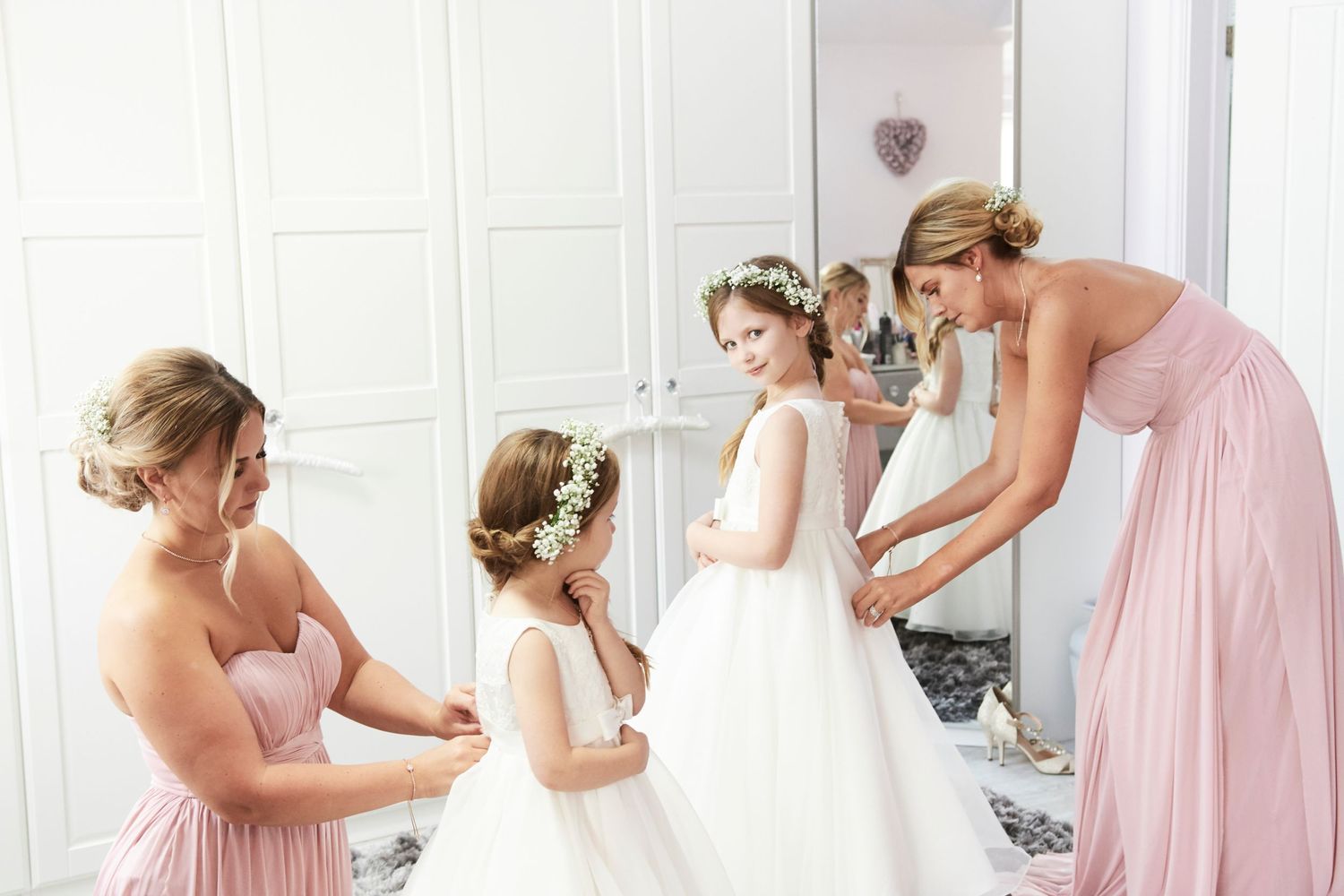 bridesmaids help flowergirls with their dresses on, by award winning Norwich wedding photographer Faye Amare