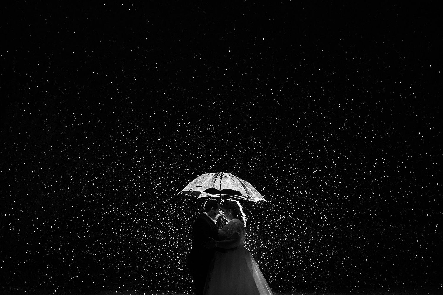 bride and groom hold an umbrella in the rain at night by Norfolk Wedding Photographer Faye Amare