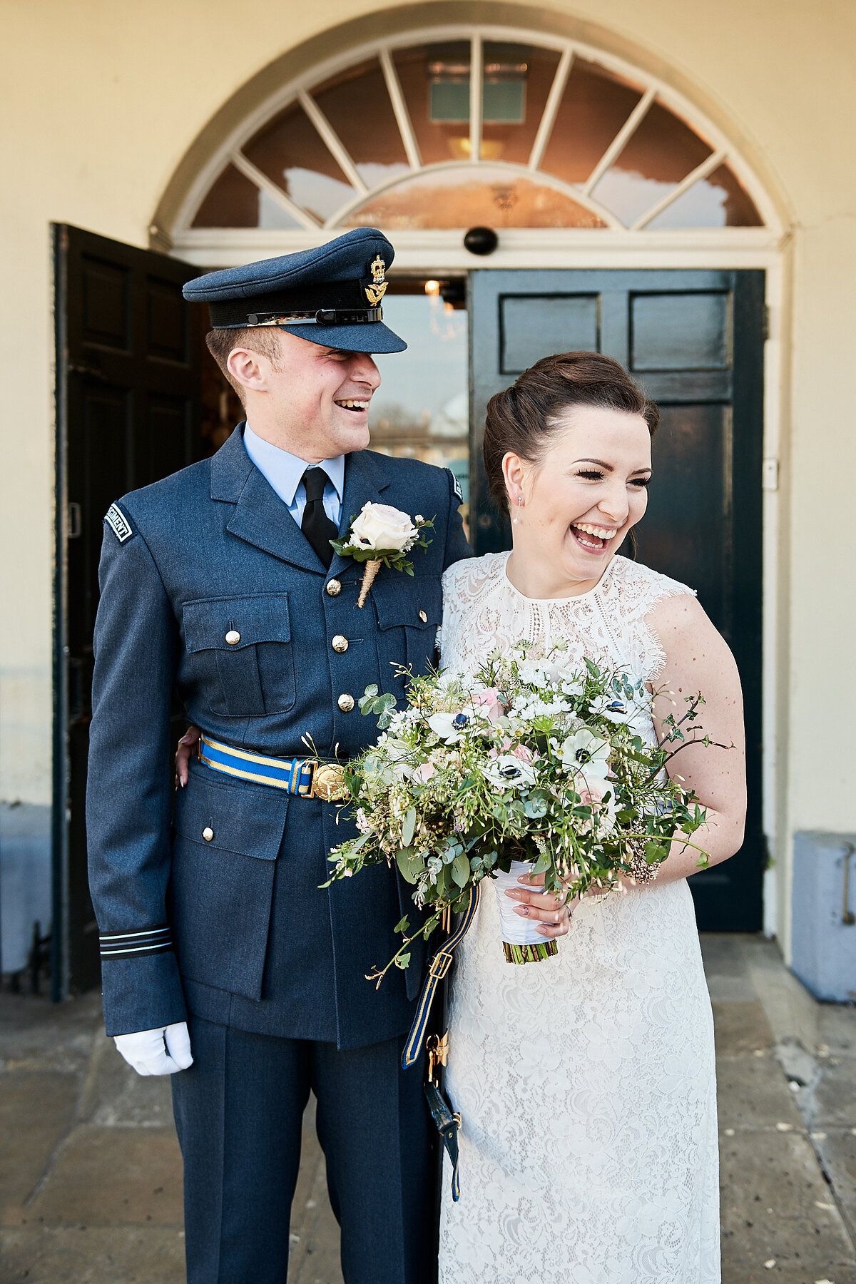 military RAF groom and bride laugh after their wedding at the athenaeum in bury st edmunds by Faye Amare